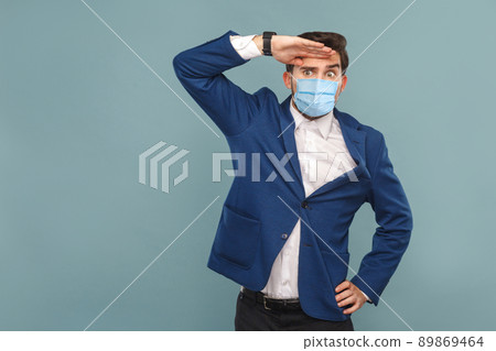 Looking so far with attention. young man with surgical medical mask, serious face looking away. Business people medicine and health care concept. Indoor, studio shot on blue background 89869464