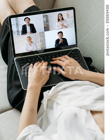 Video call. Global telework. Wfh internet conference. Relaxed woman using laptop on couch working from home online with diverse business team on screen. 89869486