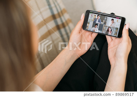 Virtual conference. Working from home. Mobile video chat. Relaxed female employee using phone on couch discussing project with diverse business team online. Virtual conference. Working from home. Mobile video chat. Relaxed female employee using phone on couch discussing project with diverse business team online. 89869517