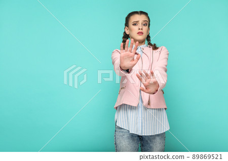 oh no, please stop. portrait of beautiful cute girl standing with makeup and brown pigtail hairstyle in striped light blue shirt pink jacket. indoor, studio shot isolated on blue or green background. oh no, please stop. portrait of beautiful cute girl standing with makeup and brown pigtail hairstyle in striped light blue shirt pink jacket. indoor, studio shot isolated on blue or green background. 89869521