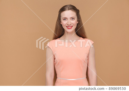 Toothy smile and happiness concept. looking at camera. portrait of emotionalmbeautiful woman with makeup and long hair in pink dress. indoor, studio shot, isolated on light brown or beige background. Toothy smile and happiness concept. looking at camera. portrait of emotionalmbeautiful woman with makeup and long hair in pink dress. indoor, studio shot, isolated on light brown or beige background. 89869530