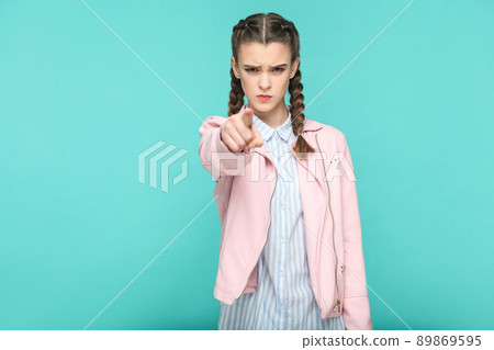 serious hey you portrait of beautiful cute girl standing with makeup and brown pigtail hairstyle in striped light blue shirt pink jacket. indoor, studio shot isolated on blue or green background. serious hey you portrait of beautiful cute girl standing with makeup and brown pigtail hairstyle in striped light blue shirt pink jacket. indoor, studio shot isolated on blue or green background. 89869595