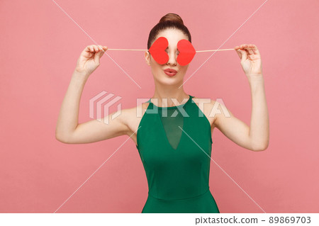 Cute woman holding two small red heart, closed eyes , kiss. Expression emotion and feelings concept. Studio shot, isolated on pink background Cute woman holding two small red heart, closed eyes , kiss. Expression emotion and feelings concept. Studio shot, isolated on pink background 89869703