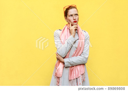 Pretty casual style girl in coat and pink scarf, got the idea and thinking. Isolated studio shot on yellow background. Pretty casual style girl in coat and pink scarf, got the idea and thinking. Isolated studio shot on yellow background. 89869808