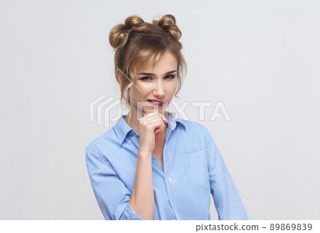 Liar blonde woman. Bite lips, flirt or thinking. Thinking of something bad. Studio shot, gray wall Liar blonde woman. Bite lips, flirt or thinking. Thinking of something bad. Studio shot, gray wall 89869839