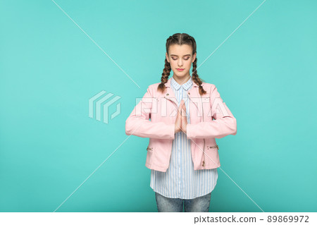 meditation and yoga portrait of beautiful cute girl standing with makeup and brown pigtail hairstyle in striped light blue shirt pink jacket. indoor, studio shot isolated on blue or green background. 89869972