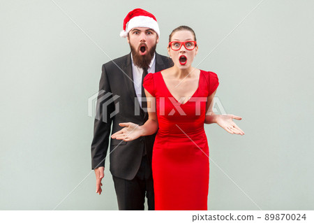 Businessman and woman looking at camera, standing together, open mouth with amazed face. Studio shot, gray background 89870024