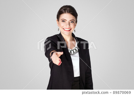 Woman in suit looking at camera and showing handshake sign. Studio shot, indoor. Isolated on grey background 89870069