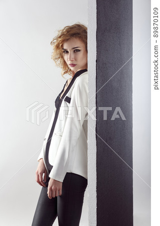 Sensuality fashion model posing near black wall undressing her white jacket and looking at camera. 89870109