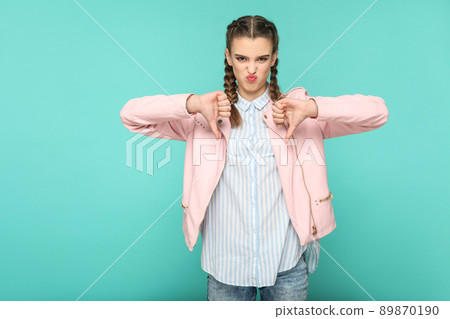 unsatisfied dislike portrait of beautiful cute girl standing with makeup and brown pigtail hairstyle in striped light blue shirt pink jacket. indoor, studio shot isolated on blue or green background. unsatisfied dislike portrait of beautiful cute girl standing with makeup and brown pigtail hairstyle in striped light blue shirt pink jacket. indoor, studio shot isolated on blue or green background. 89870190