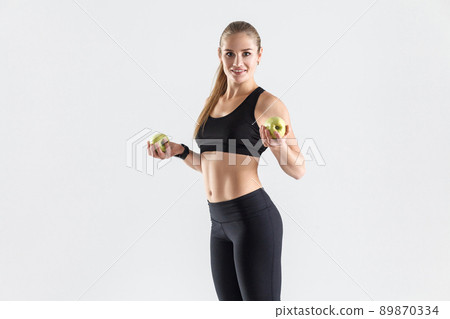Healthy food, fresh food, diet concept. Athletic woman holding organic green apple, toothy smiling and looking at camera Healthy food, fresh food, diet concept. Athletic woman holding organic green apple, toothy smiling and looking at camera 89870334