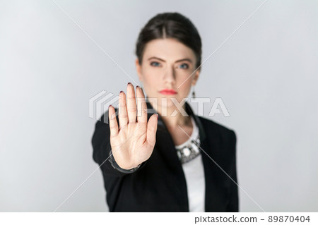 Focus on hand. Seriously woman showing stop hand sign. Studio shot, indoor. Isolated on grey background 89870404