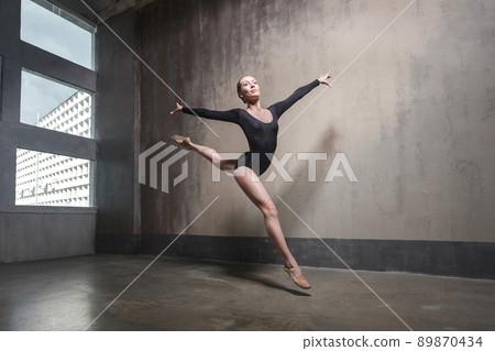 Beautiful graceful ballerine in black practice ballet positions near large window in light hall. Ballet class training. Studio shot, gray background Beautiful graceful ballerine in black practice ballet positions near large window in light hall. Ballet class training. Studio shot, gray background 89870434