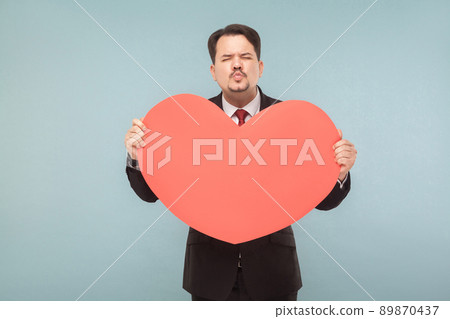 Love, st. valentine's concept. Businessman holding big heart, send kiss. Indoor, studio shot, isolated on light blue or gray background 89870437