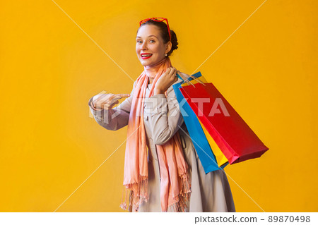 Young adult woman pointing finger on bags and looking at camera and toothy smile. On yellow background. Studio shot 89870498