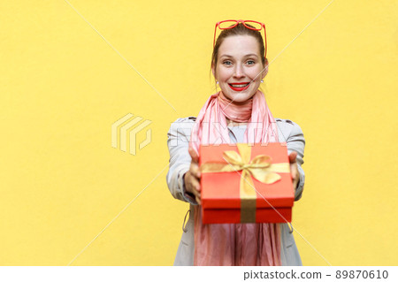 Its for you. Delivery woman holding a box. Studio shot on yellow background 89870610