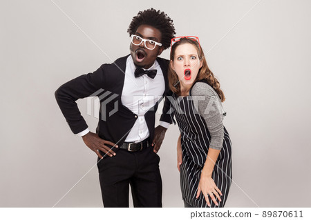 Friends looking at camera with open mouth and shocked face. Studio shot, gray background 89870611
