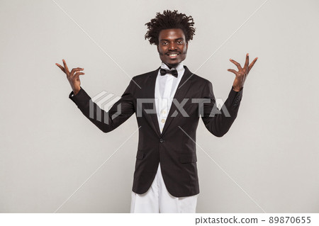 African well dressed singer or actor with afro hair style in classic style tuxedo and bow tie toothy smiling. Indoor, isolated studio shot on gray background 89870655