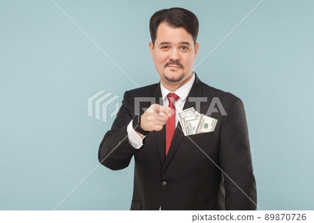 Handsome businessman pointing finger at camera with little smile. Indoor, studio shot, isolated on light blue or gray background Handsome businessman pointing finger at camera with little smile. Indoor, studio shot, isolated on light blue or gray background 89870726