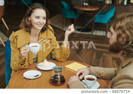 Portrait of serious modern guy with beard sitting at round table in loft cafe and calling by mobile phone Portrait of serious modern guy with beard sitting at round table in loft cafe and calling by mobile phone 89870754