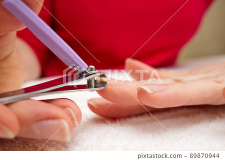 Woman Clipping Nail s with Forceps. Female cuts his nails on a white background with tweezers for nails. manicure procedures yourself at home 89870944