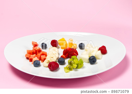 Fresh fruit salad on white plate. Mixed fruit in white plate healthy food style. Useful fruit salad of fresh fruits and berries on pink background Fresh fruit salad on white plate. Mixed fruit in white plate healthy food style. Useful fruit salad of fresh fruits and berries on pink background 89871079