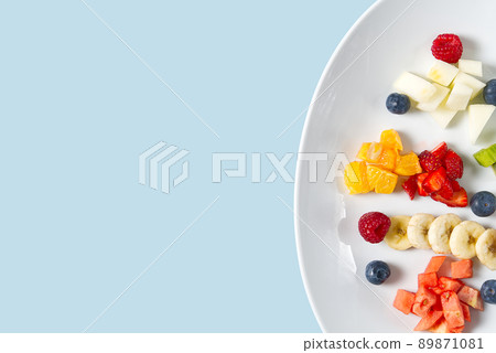 Fresh fruit salad on white plate. Mixed fruit in white plate healthy food style. Useful fruit salad of fresh fruits and berries on light blue background 89871081