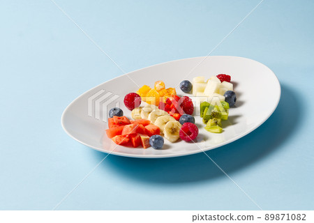 Fresh fruit salad on white plate. Mixed fruit in white plate healthy food style. Useful fruit salad of fresh fruits and berries on light blue background 89871082