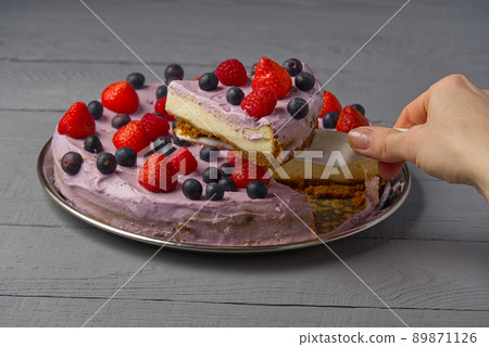 Woman divided cheesecake and take one slice to offer it. Home made Cheesecake with Strawberry, blueberry and raspberry on grey wooden background. Woman divided cheesecake and take one slice to offer it. Home made Cheesecake with Strawberry, blueberry and raspberry on grey wooden background. 89871126