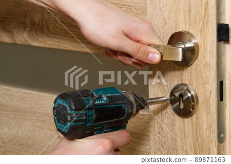 handyman repair the door lock in the room. man repairing the door handle furniture. carpenter at lock installation with electric drill into interior wood door 89871163