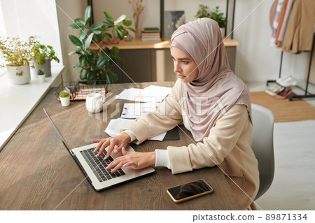 Middle Eastern businesswoman wearing stylish hijab and abaya working on laptop in modern workplace, high angle shot 89871334