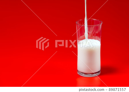 milk is poured into a glass transparent glass on a red background. 89871557