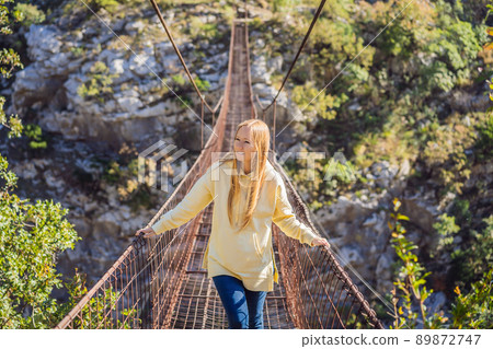 Woman tourist on Old rusty bridge. Attraction Long extreme suspension iron bridge across the river Moraca. Sights of Montenegro. Landmark Montenegro Woman tourist on Old rusty bridge. Attraction Long extreme suspension iron bridge across the river Moraca. Sights of Montenegro. Landmark Montenegro 89872747