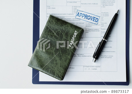 Top-down flat lay of passport in dark green leather cover, travel visa application paper with approved seal on it and pen on table, copy space 89873317
