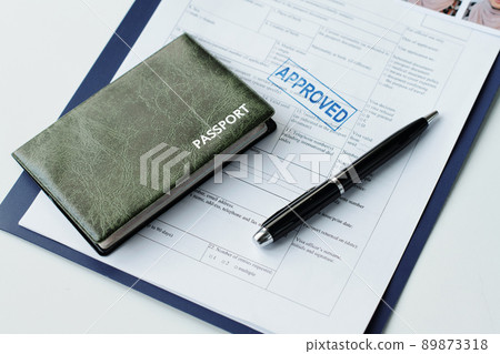 High angle close-up of passport in leather cover, travel visa application paper with approved stamp on it and pen on table 89873318