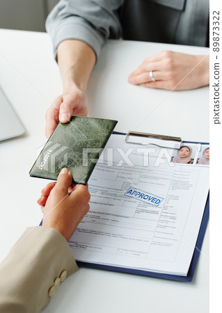 High angle of unrecognizable consular officer returning passport to Muslim woman after visa application approval 89873322