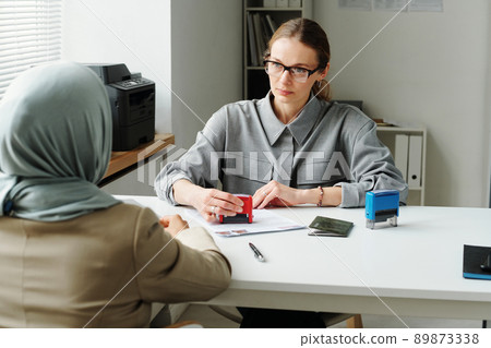 Horizontal shot of Caucasian woman working as consular officer rejecting visa application for Muslim woman for some reasons 89873338