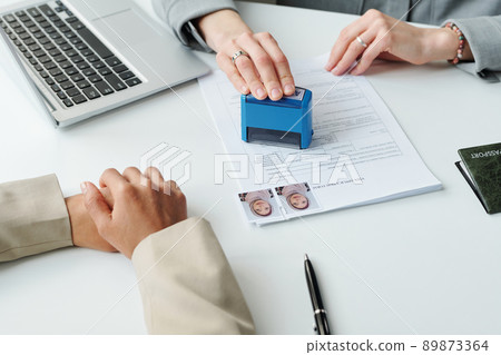 Medium close-up shot of unrecognizable consular officer putting approval seal on visa application form for Muslim woman after interview 89873364