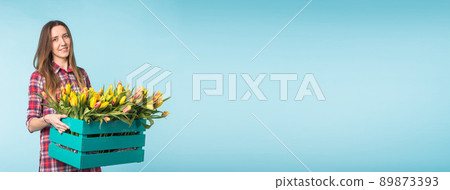 Happy caucasian young woman holding box with tulips banner on blue background with copy space and place for advertising Happy caucasian young woman holding box with tulips banner on blue background with copy space and place for advertising 89873393