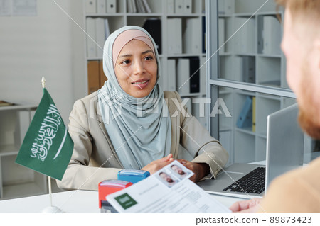 Modern Muslim woman wearing hijab working as consular officer in Saudi Arabia embassy interviewing Caucasian man for visitor visa 89873423