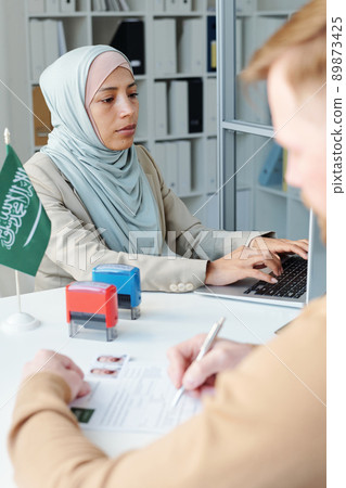 Selective focus shot of Muslim woman wearing hijab working as consular officer in embassy having appointment with unrecognizable man 89873425