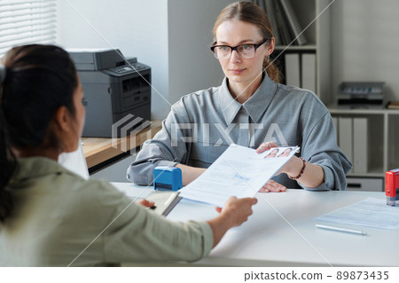 Mature Caucasian female consular officer sitting at desk in front of applicant for travel visa giving approval after successful interview 89873435