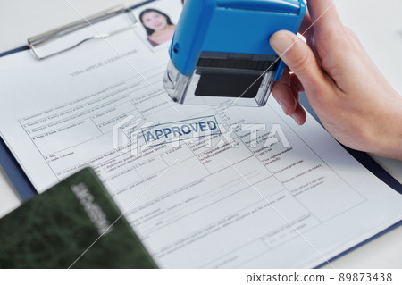 Close-up shot of unrecognizable person working as consular officer in embassy approving visa application putting seal on it Close-up shot of unrecognizable person working as consular officer in embassy approving visa application putting seal on it 89873438