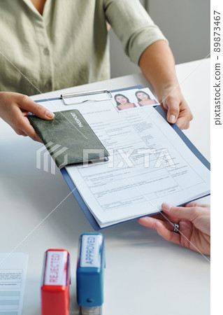 Vertical high angle of unrecognizable woman applying for work visa giving set of documents to consular officer 89873467