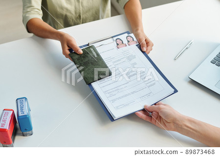 High angle of unrecognizable woman applying for travel visa in embassy giving passport and application form to consular officer 89873468