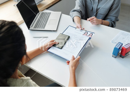 High angle view of unrecognizable woman applying for visa in embassy office giving passport and application form to consular officer 89873469