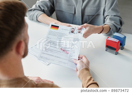 High angle view of unrecognizable consular officer returning visa application form paper with rejected stamp on it to applicant 89873472