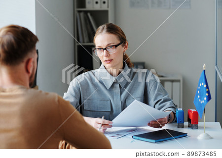 Mature woman working as consular officer in embassy interviewing unrecognizable man sitting in front of her for schengen visa 89873485