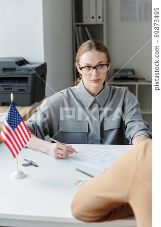 Vertical shot of serious woman working in US embassy or consulate interviewing unrecognizable person for visa 89873495