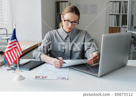 Mature woman working In US embassy sitting at desk in office looking through data in visa application papers 89873512